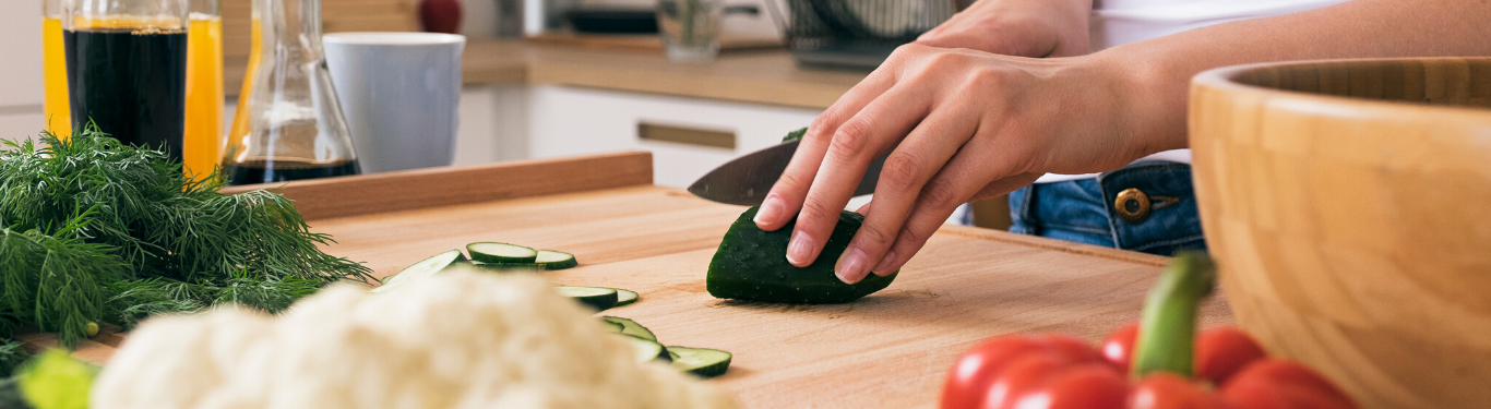 Hands slicing fresh vegetables on a wooden cutting board